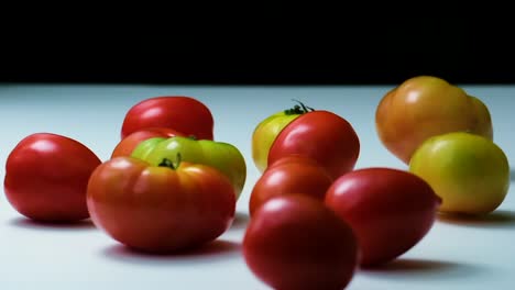 slow motion shot of a variety of big tomatoes rolling back and forth on a white surface