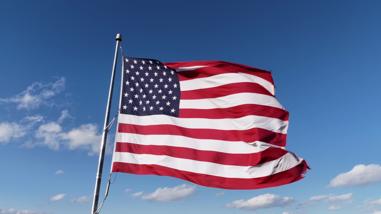 Vajende patriotisk amerikansk flag mod blå himmel og sollys. Nærbillede fra luften i USA. En stolt nation. Striber og stjerner i rød, blå og hvid farve. Luftfoto.
