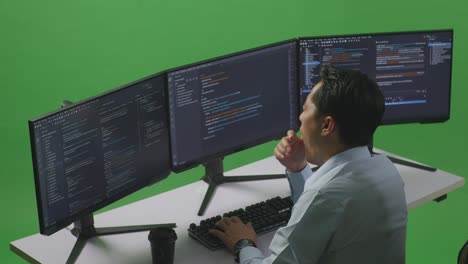 Side View Of Tired Asian Man Developer Yawning Before Sleeping While Write Code With Multiple Computer Screens In Green Screen Studio