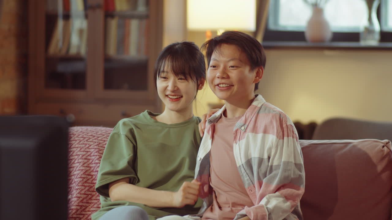 家でテレビを見て笑うアジア人女性カップル