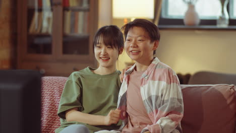 asian female couple watching tv and laughing at home