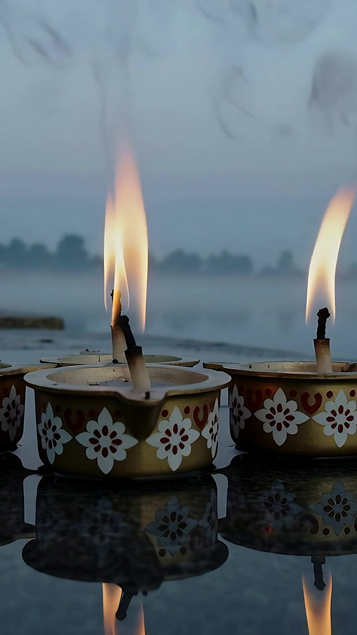 Vertical video: Tilting by gust three decorative diyas flickering on shiny stone at dawn