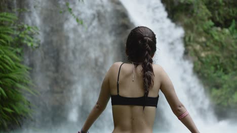 hermosa mujer en bikini negro mira hacia una hermosa cascada tropical en el bosque