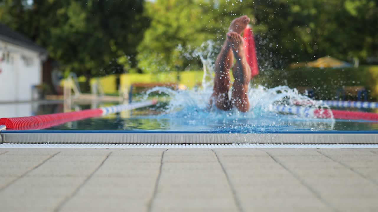 Slider shot of a swimmer's legs as he jumps into the water beautiful green scenery background