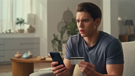 Man looks surprised while holding a credit card and phone