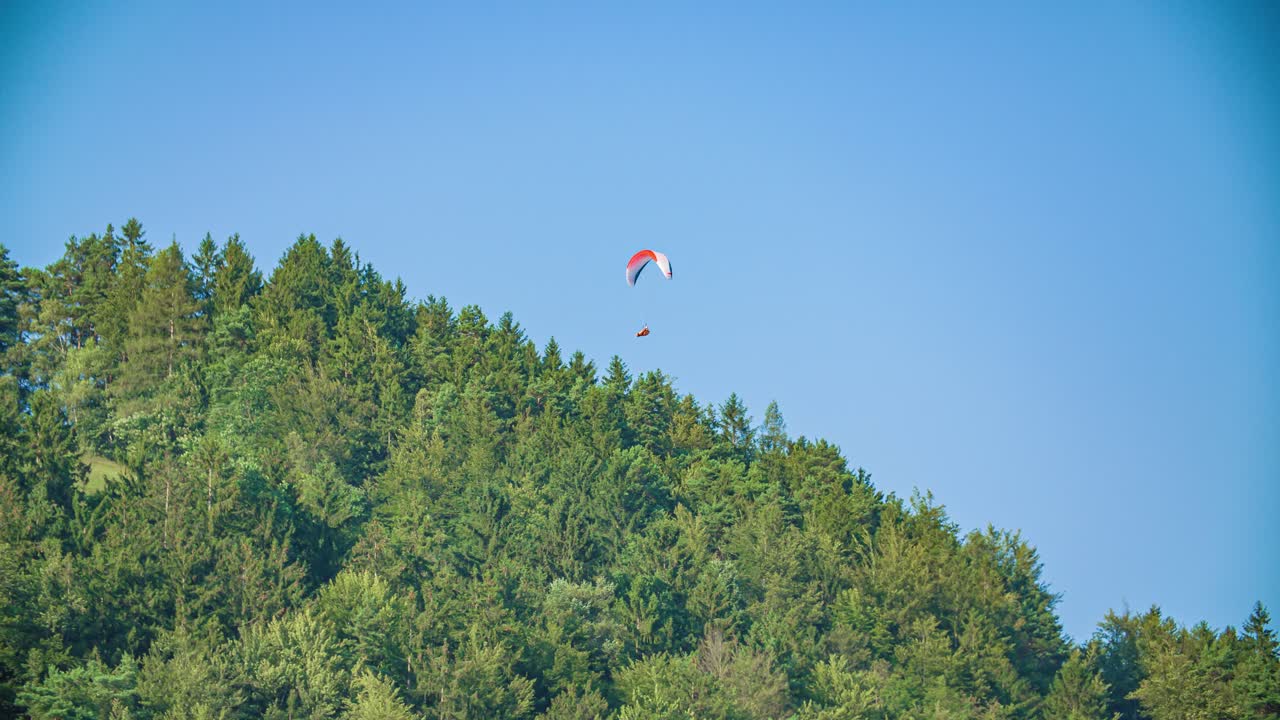 Hang glider soars high above valley, near tree covered hillside