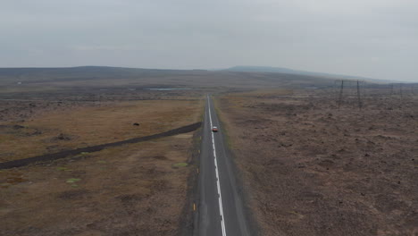 Drone-view-4x4-car-driving-along-motorway-in-wild-countryside-in-Iceland.-High-angle-view-icelandic-majestic-mossy-highlands-with-car-driving-along-ring-road,-icelandic-most-important-highway