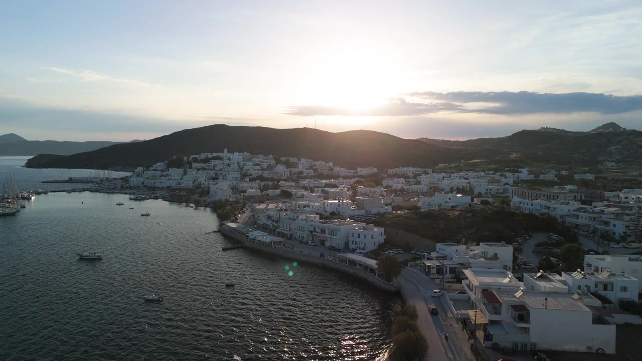 Volo di drone in ascesa al tramonto sopra il villaggio di Pollonia nell'isola di Milos, Grecia, che rivela il paesaggio greco.