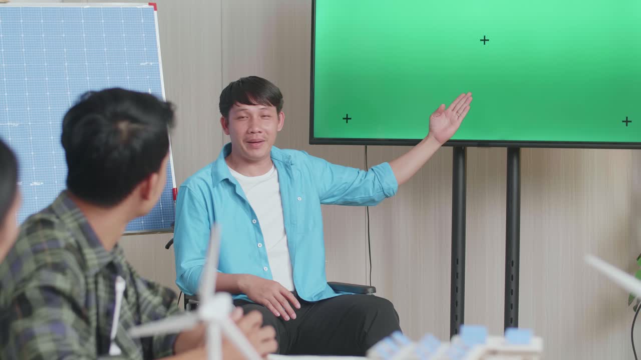 체어에 앉아 태양전지를 쓴 아시아인 엔지니어가 사무실에서 녹색 스크린 tv에 대한 프레젠테이션을 성공적으로 진행하면서 관객들은 박수를 치며 인상적이라고 느다.