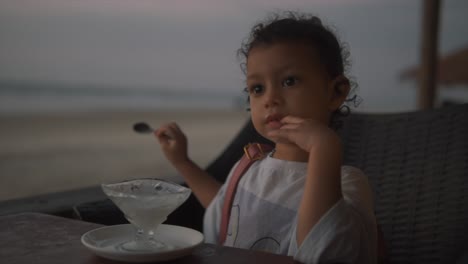 little-cute-girl-enjoying-ice-cream-and-playing-while-sitting-in-a-restaurant-on-a-beach