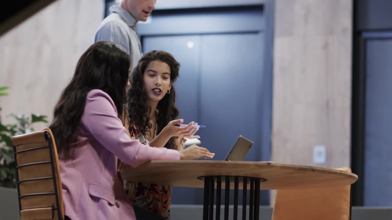 Diverse male and female colleagues in discussion using tablet in casual office meeting, slow motion
