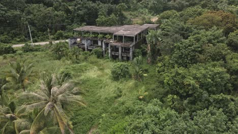 aerial backwards dolly shot of derelict abandoned small hotel building on a tropical island with palm trees