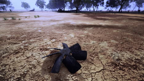 broken fan blade rests on cracked ground in remote landscape during daylight