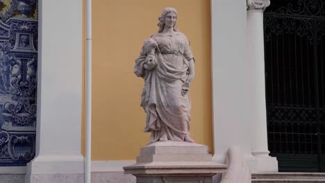 estatua de mujer sosteniendo un busto con edificio en segundo plano.