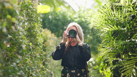 Blonde-Fotografin-Lacht-Und-Fotografiert-Mit-DSLR-Kamera-Im-Garten,-Zeitlupe-Mit-4K-Auflösung