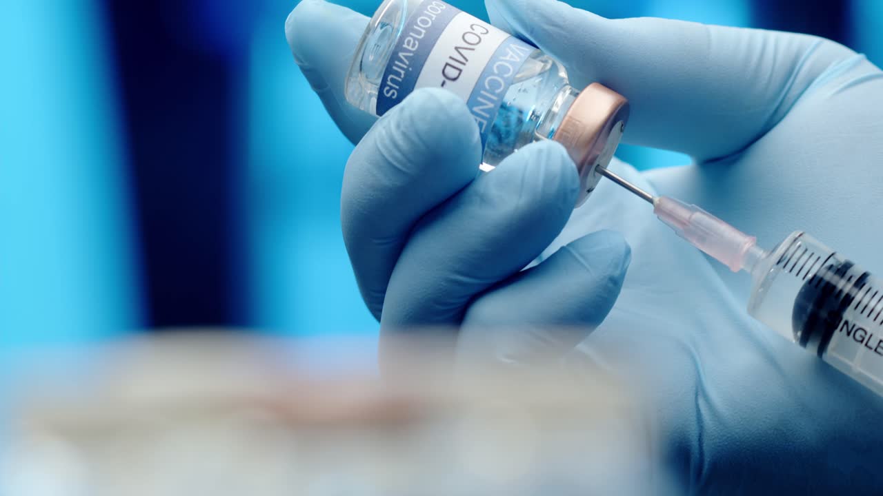 A doctor or nurse wearing latex gloves fills a syringe with the COVID vaccine - isolated close up