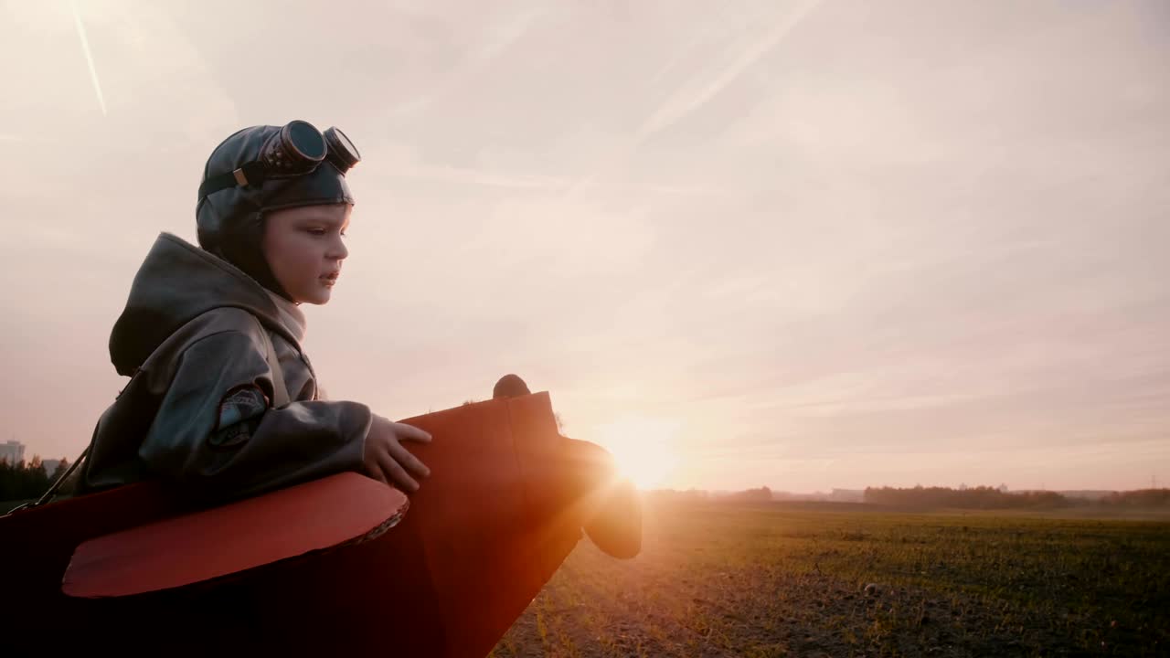 La telecamera laterale segue un bambino pilota felice con un divertente costume da aereo che corre in un incredibile campo autunnale al tramonto, slow motion