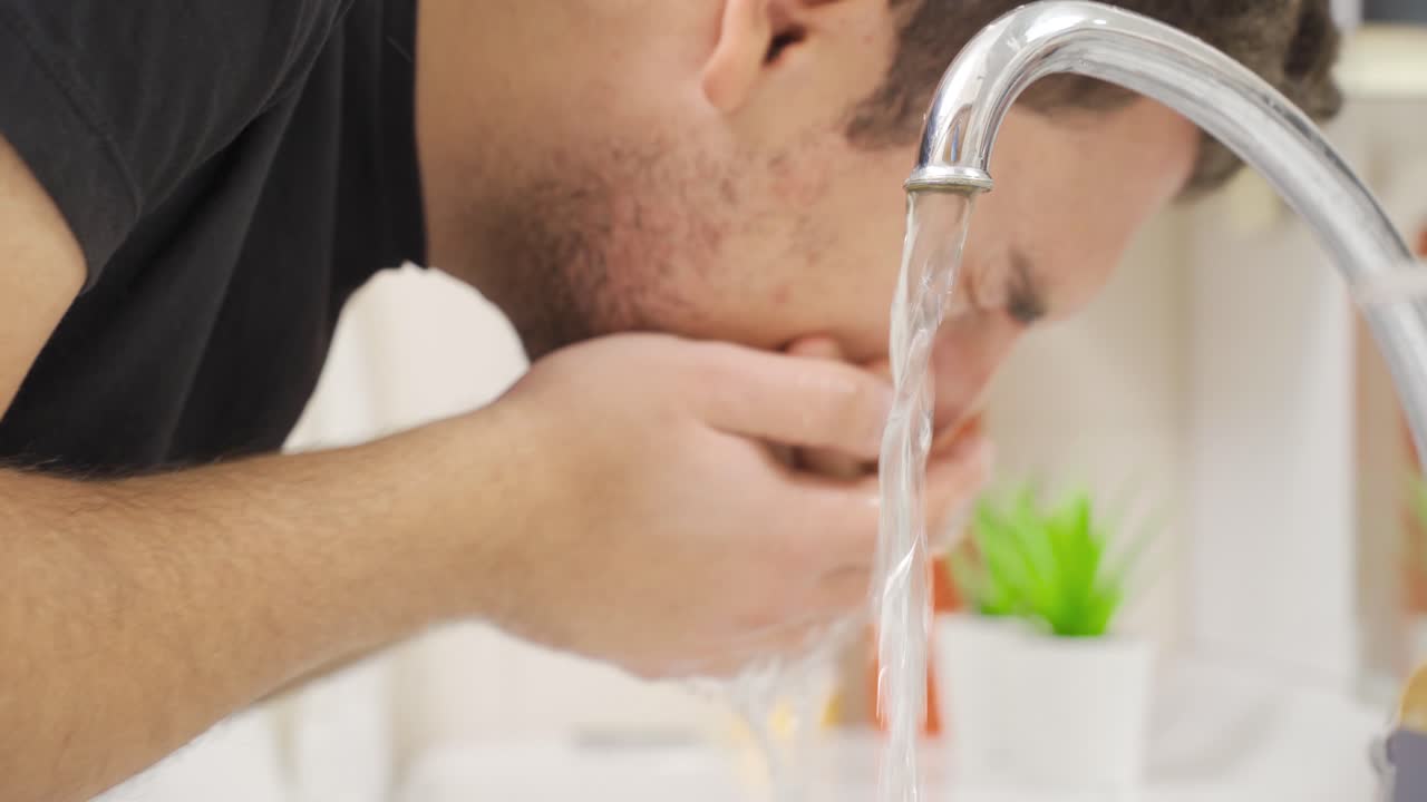 Young man washes his face in the sink with cold water.