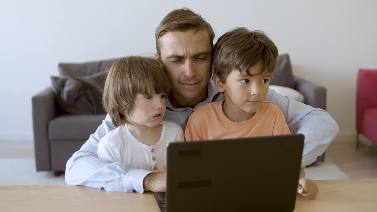 papá serio trabajando en la computadora portátil y abrazando a sus hijos