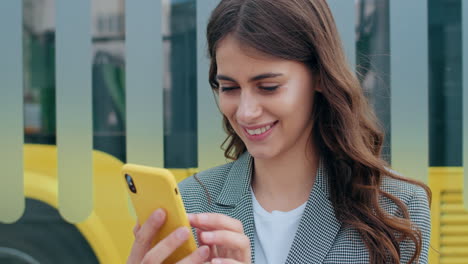 close-up of a smiling young woman using a yellow smartphone outdoors