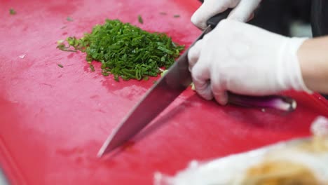 las manos del chef cortando cebolla verde en la tabla de cortar roja, de cerca