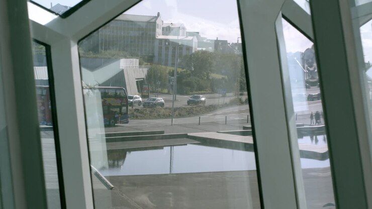 Un autobús turístico rojo pasa junto a una vista urbana a través de ventanas de cristal geométricas en Islandia.
