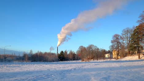 white smoke coming out of a tall chimney on a cold sunny winter day with a clear blu sky