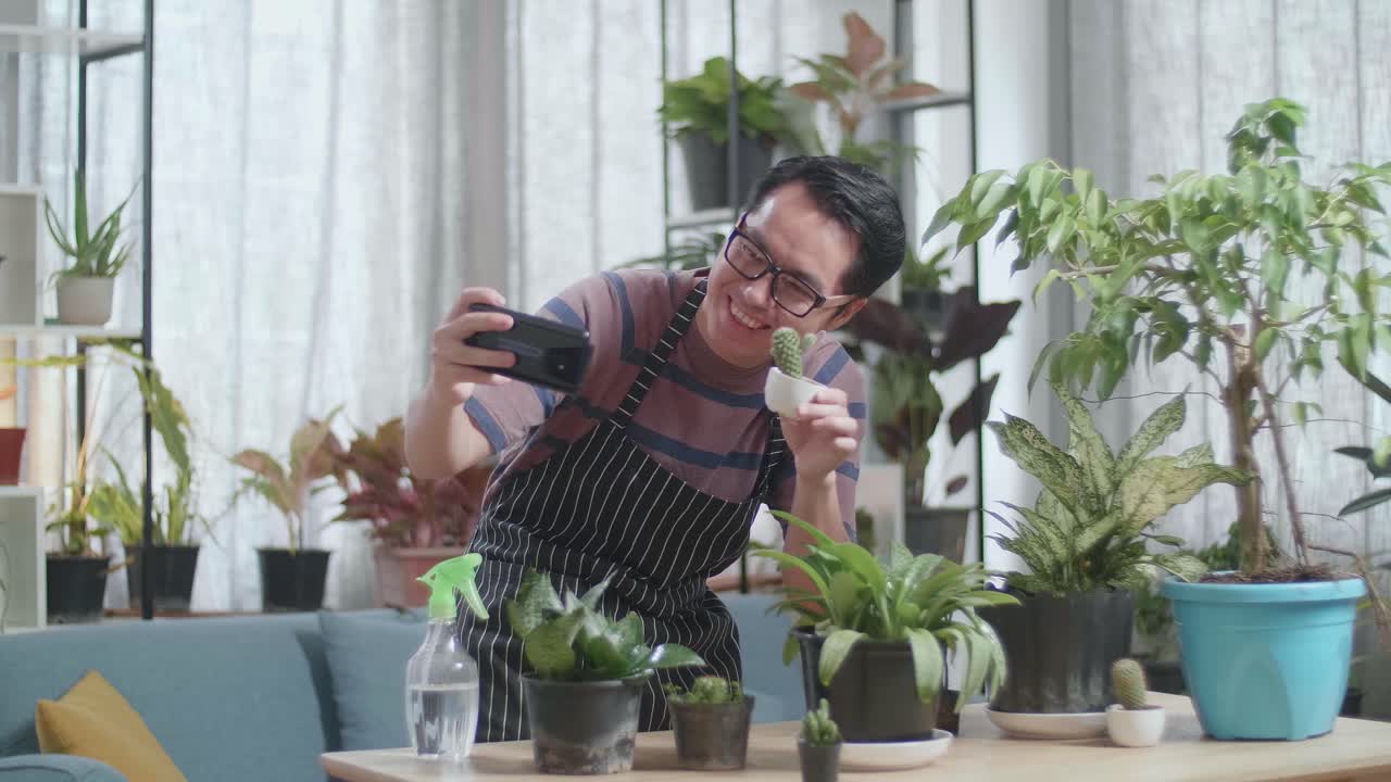 식물 을 들고 있는 아시아인 남자 가 집 에서 스마트폰 으로 사진 을 찍고 있다