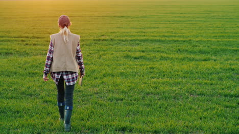 Una-Joven-Campesina-Camina-Por-Un-Campo-De-Trigo-Con-Una-Tableta-Vista-Trasera