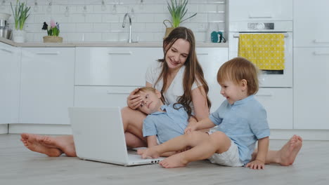 hermosa familia joven moderna acostada en el suelo en casa y haciendo algo en la computadora portátil