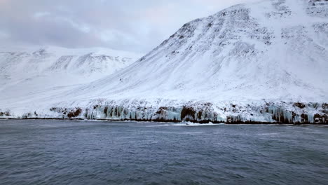 grandes olas rompen al pie de las altas montañas nevadas de islandia