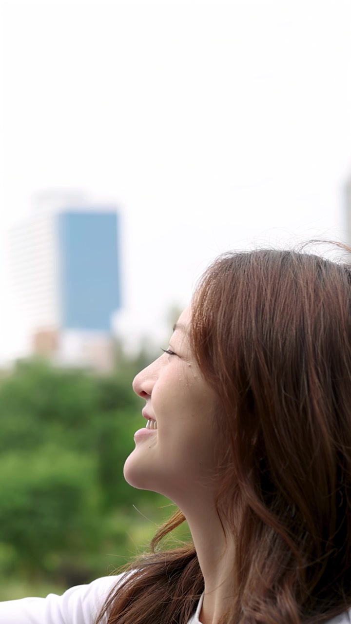 Close-up profile of a happy Asian woman smiling outdoors with a soft city background