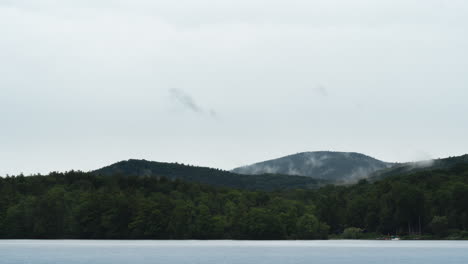 cloudy green mountain range with cloud cover over looking foggy lake