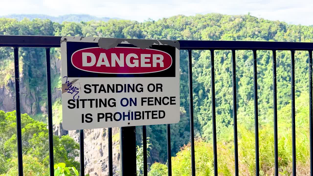 Camera pans from warning sign to lush forested cliffs under bright, natural daylight conditions