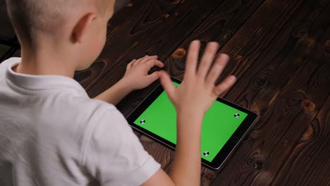 primer plano de un niño sosteniendo una tableta con una pantalla verde sobre un fondo de madera.