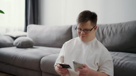 Young-man-with-down-syndrome-using-smartphone-and-credit-card-sitting-on-the-floor