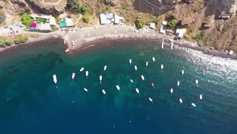 Vista-Aérea-Estática-De-Arriba-Hacia-Abajo-De-Muchos-Barcos-De-Pesca-En-El-Mar-Mediterráneo-Con-Agua-Azul-Cristalina-Y-Playa-Santorini,-Grecia