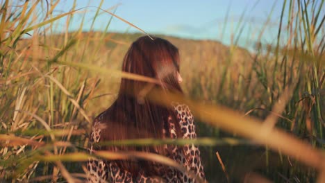 caucasian brunette woman wearing stylish animal pattern dress walking alone in tall green feather grass field, turns and smiles looking at camera, close up portrait