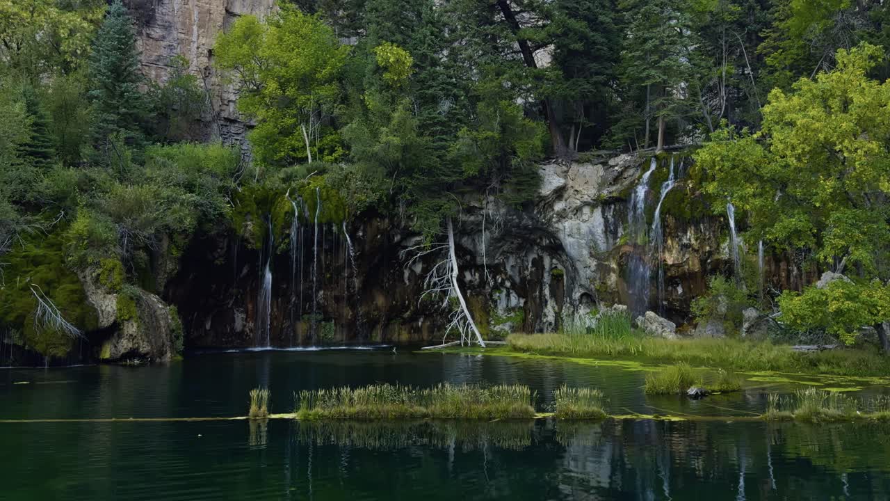 Superfície do Lago Suspenso brilhando com reflexos de árvores verdes e bordas rochosas próximas, estabelecendo estática