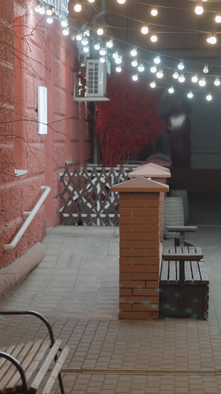 una acogedora escena al aire libre de la noche con luces de cuerda iluminando un camino alineado con bancos y una pared de ladrillo