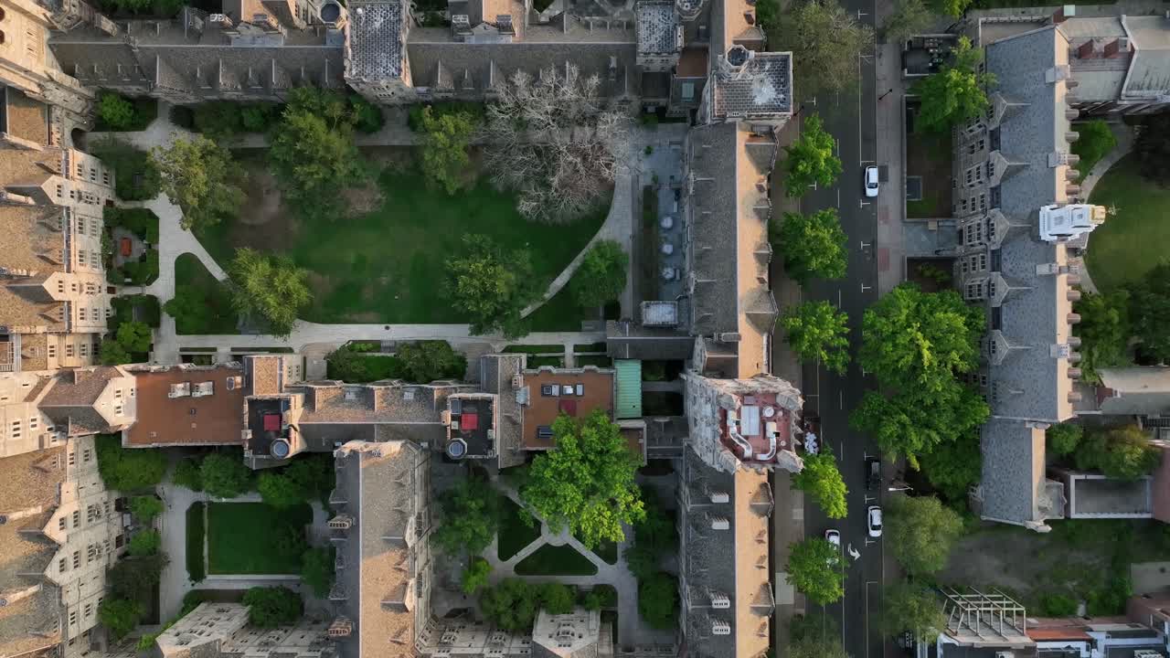 White car on street beside historic neo gothic Yale university in New Haven, Connecticut. Aerial top down flyover. Green grass inside inner yard of campus. Historic college area in small town