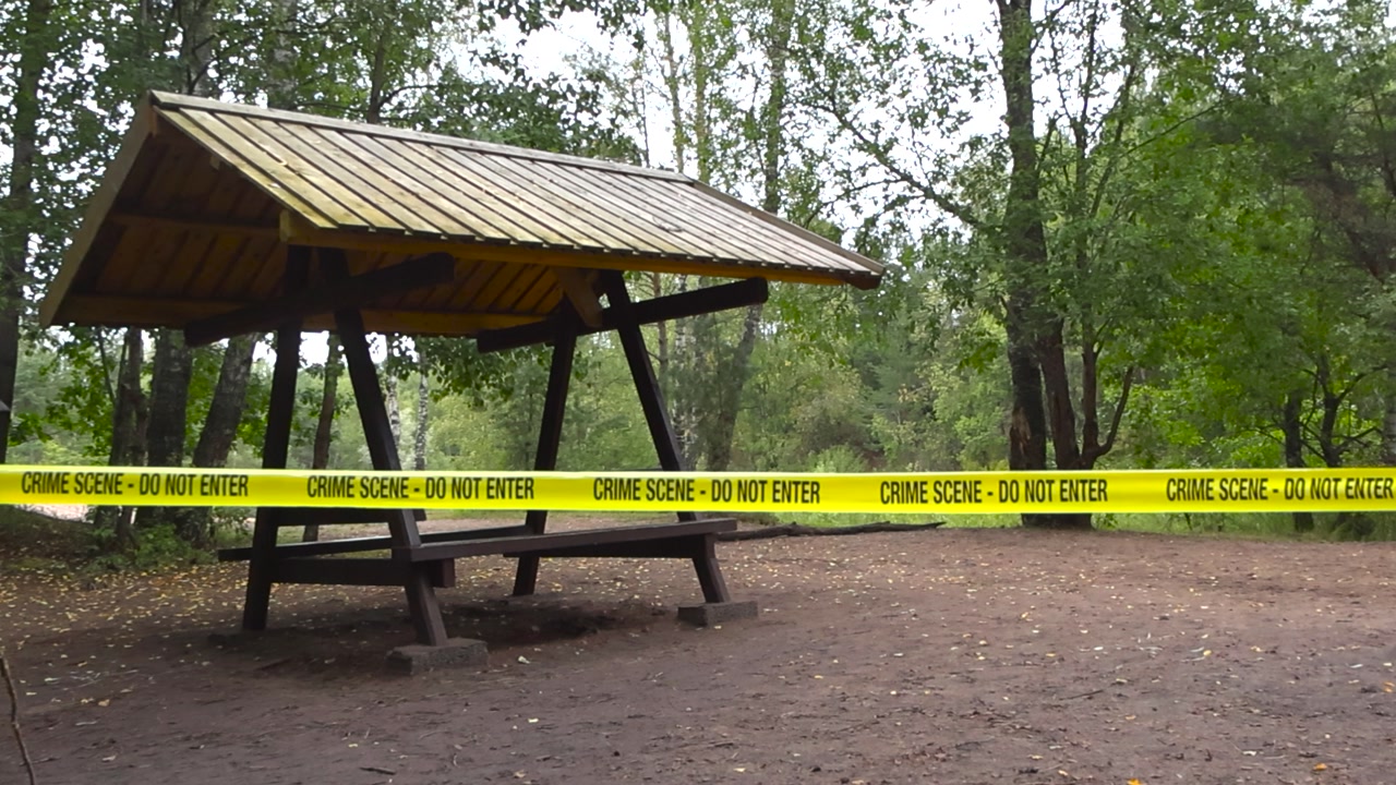 Yellow police line or Crime scene forensics investigation tape ribbon pulled in front of a outdoors camping area with a lake or a river in the forest background. Tape is in focus, background bokeh.