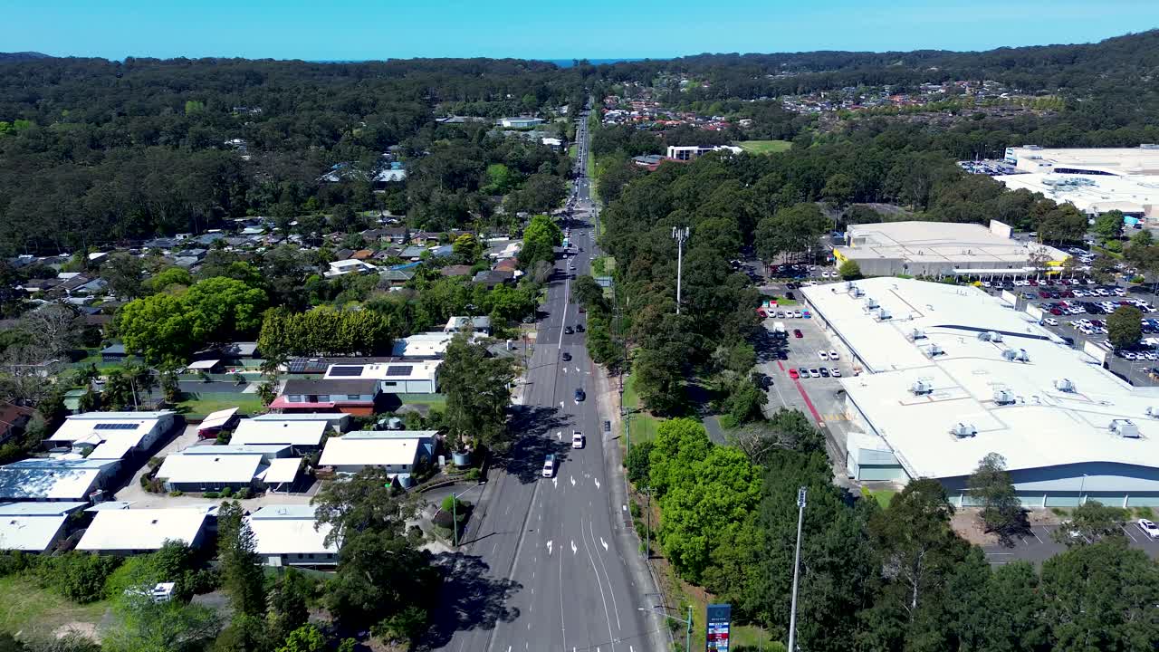 Drone aerial landscape of cars driving along main road town highway with retail shopping village and bushland trees at Erina on the Central Coast NSW Australia transport tourism retail infrastructure