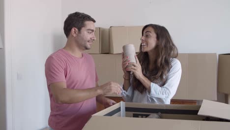 happy couple unpacking cardboard boxes with stuff, talking and smiling