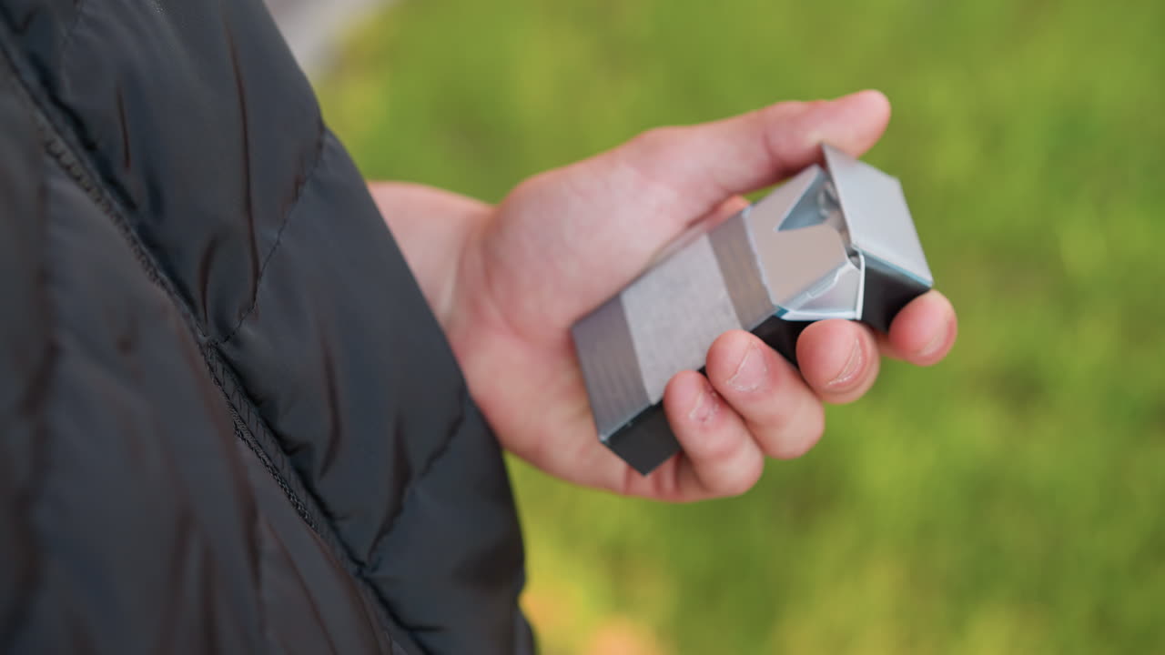close up of man wearing puffer jacket discarding burning cigarette into waste bin beside green grass as he makes firm decision to quit smoking outdoors under golden sunlight