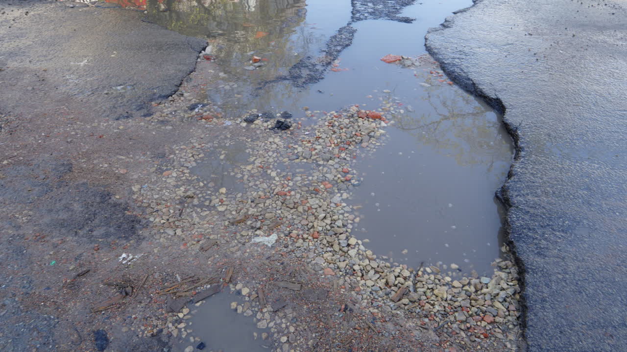 Plassen en scheuren in de weg door slecht wegonderhoud, versleten asfalt.