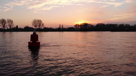 silhouette of floating buoy in river during against orange sunset skies with barge in background