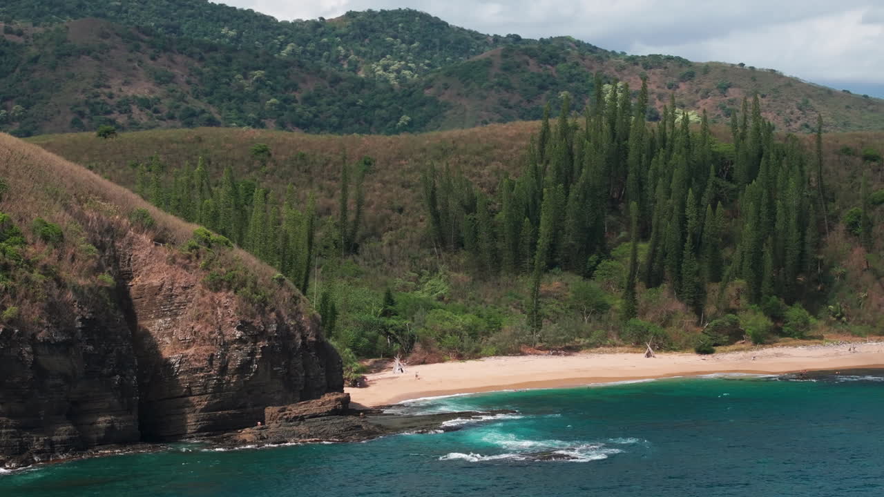 Aerial shot of Turtle Bay near Gouaro, New Caledonia, with sandy shoreline, pine-covered cliffs and deep blue waters of the South Pacific