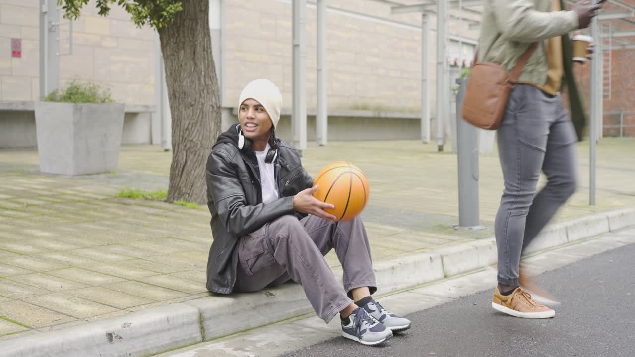 Diverse male friends checking smartphone greeting then spinning basketball on finger at plaza