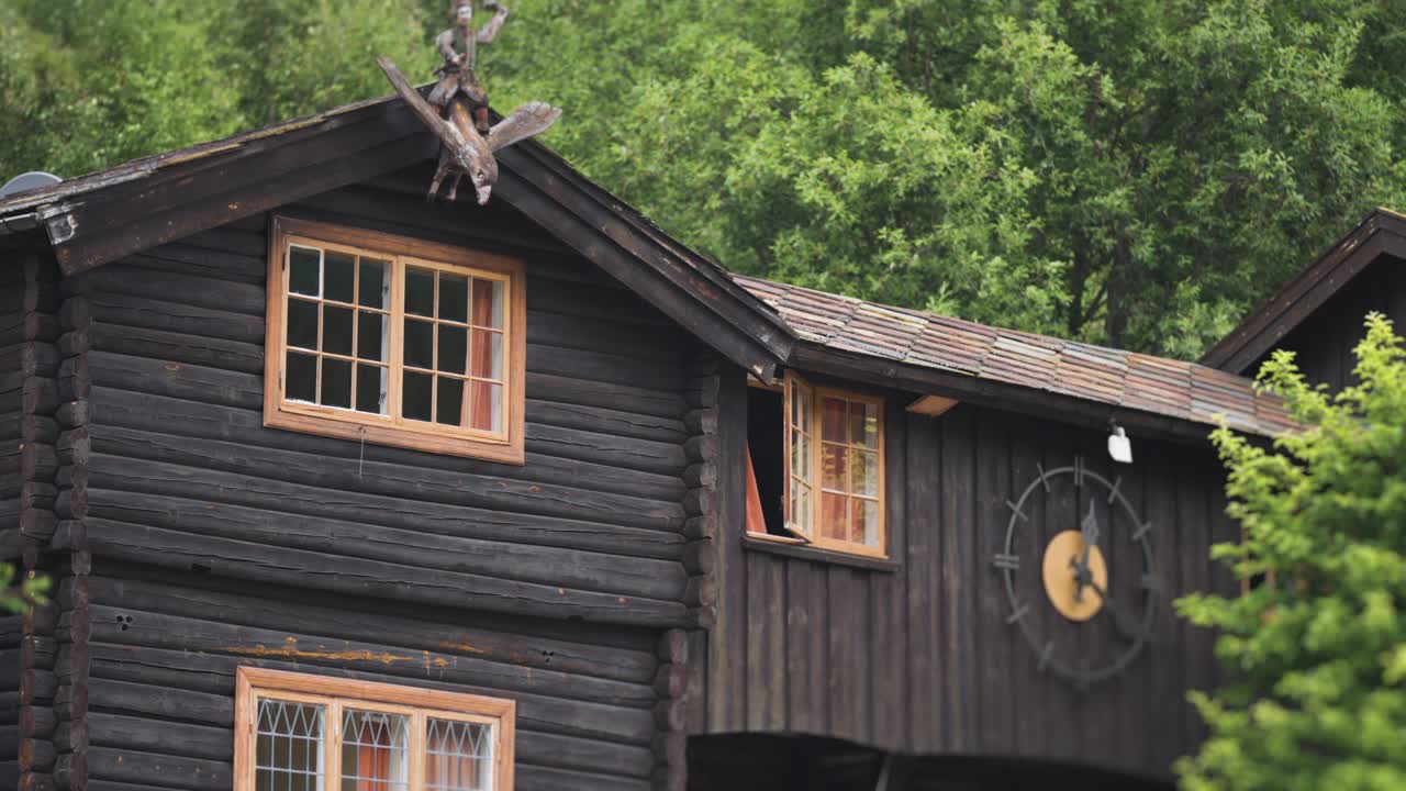 A wooden building in the Elveseter hotel complex stands amidst lush greenery, with a rustic exterior and visible clock.